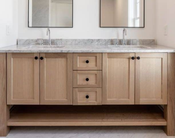 Brightly lit bathroom with dual sinks, and a gray marble countertop and shower