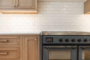 Closely cropped photo of a black oven with double doors and an induction stovetop. It sits flush against walnut cabinets with a white quartz countertop, and below a backsplash of white subway tile.