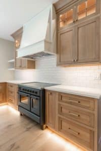 high end kitchen designs with white wooden range hood above a double range, flanked by stained walnut upper and lower cabinets. The backsplash is white subway tile.