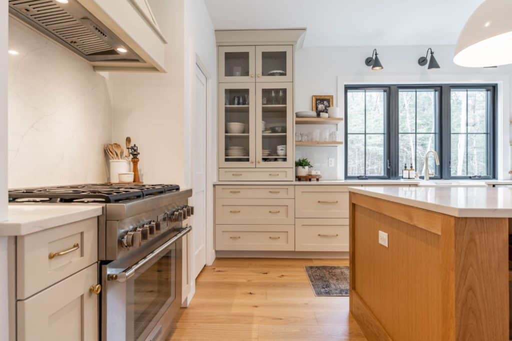 The corner of a kitchen filled with neutrals and earth tones. A glass-fronted cabinet stretches to the ceiling.